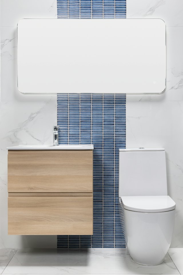 Een badkamer met een strook blauwe tegels achter het toilet en een houten badmeubel
