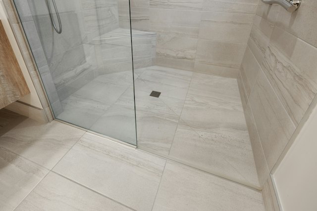 Een lichte tegelvloer die doorloopt in een douche met glazen wand